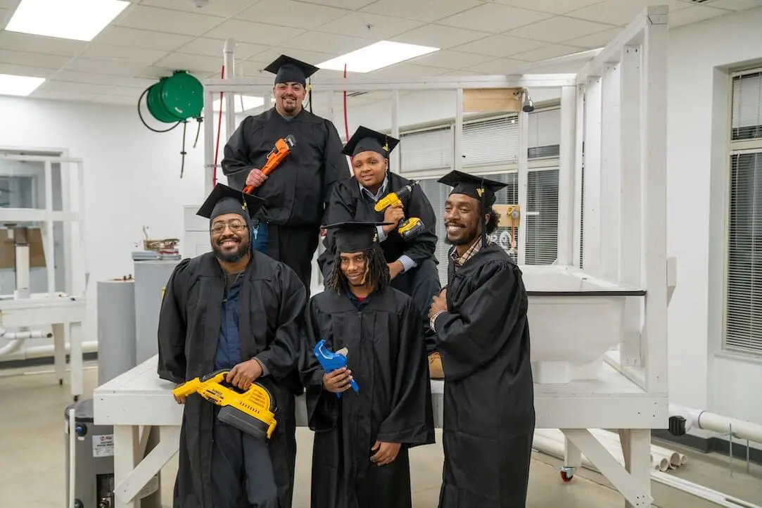 Five graduates in black caps and gowns pose indoors, holding colorful toy blasters and smiling in a laboratory setting, ready to take on in-demand careers.