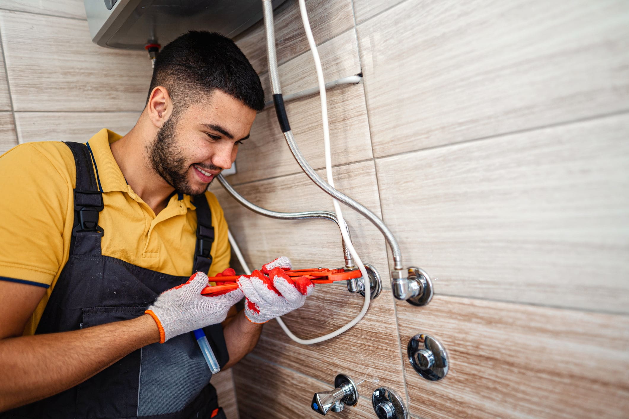 A portrait of a plumber wearing gloves, deftly adjusting a pipe with a wrench in a tiled room during work hours.